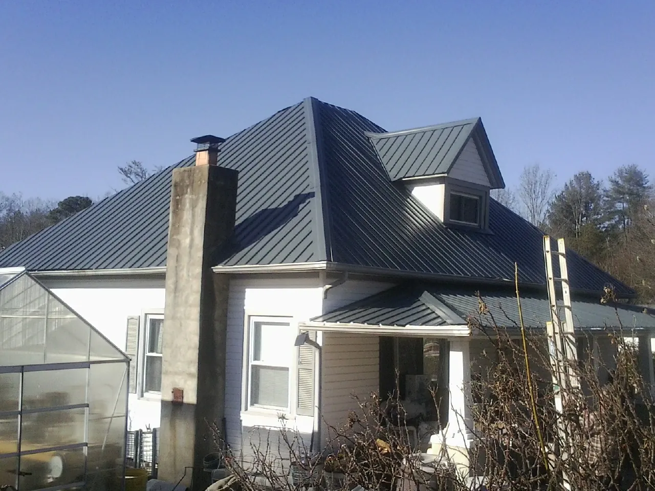 Dark blue standing seam metal roof on a white farmhouse with dormer — Slate & Tile Roof Repair by Roofing Brothers in East Helena