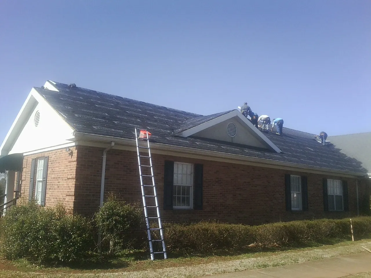 Crew tearing shingles off a brick ranch roof with a ladder set — Emergency Roof Repair work by our crew in East Helena