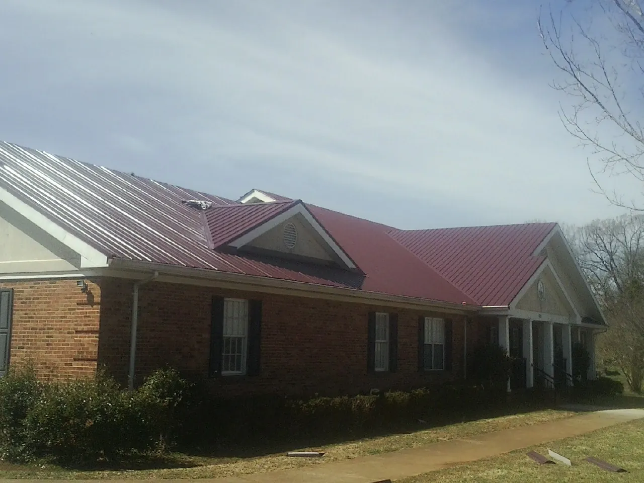 Red metal roof with gabled entries on a long brick building, from a Hail Damage Roof Repair job in East Helena