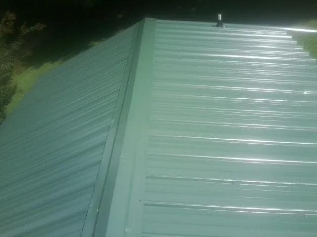 New green metal panels meeting at the ridge of a roof — Flat Roof Repair work by our crew in East Helena