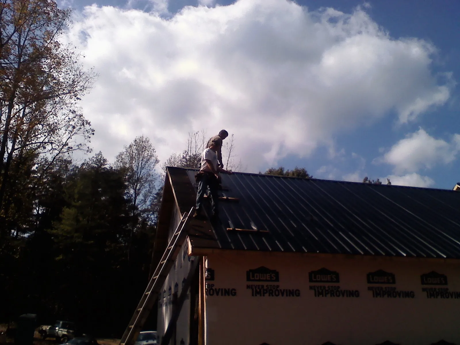 Roofer fastening dark metal panels high against a cloudy sky, from a Roof Inspection job in East Helena