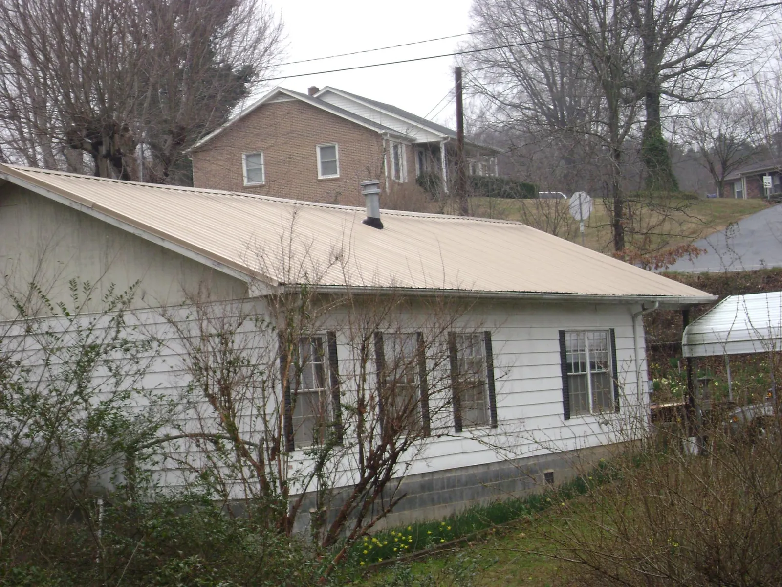 Tan metal roof on a white sided house set into a hillside — Commercial Roofing by Roofing Brothers in East Helena